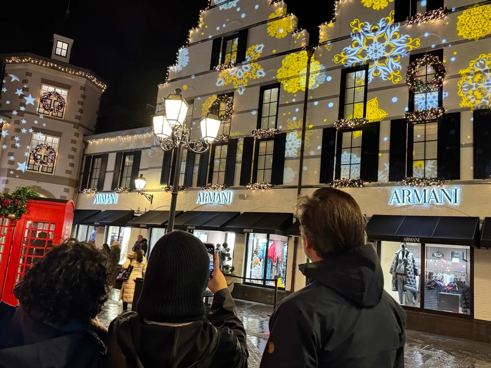 Geprojecteerde gele en blauwe sneeuwvlokken op de gevel van een winkel in Designer Outlet tijdens Lights On