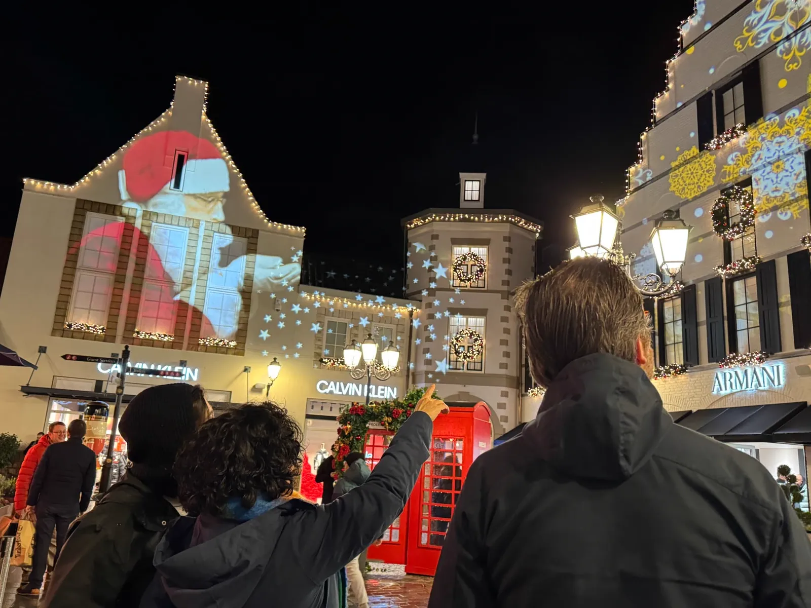 Bezoekers van Lights On bij een gevel van Designer Outlet met een geprojecteerde kerstman en sterren