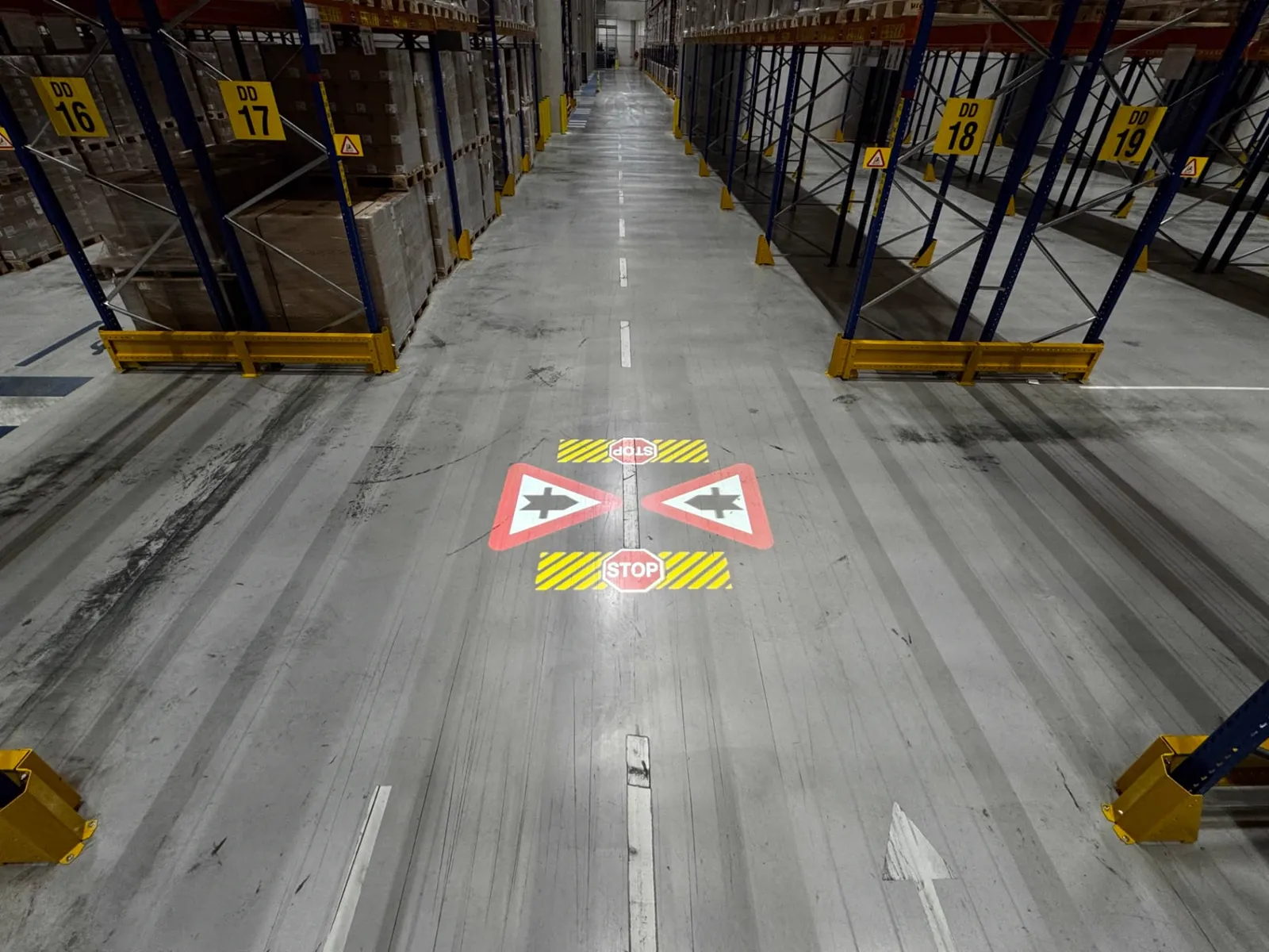 Geprojecteerde stopstrepen en voorrangsborden op de vloer van een gangpad in het magazijn van Kuehne+Nagel