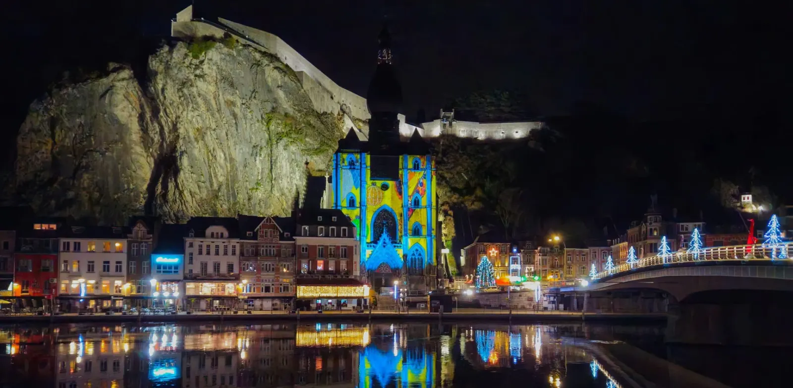 Stad Dinant bij nacht met kleurrijke projectie op de collegiale kerk en weerspiegeling in de Maas