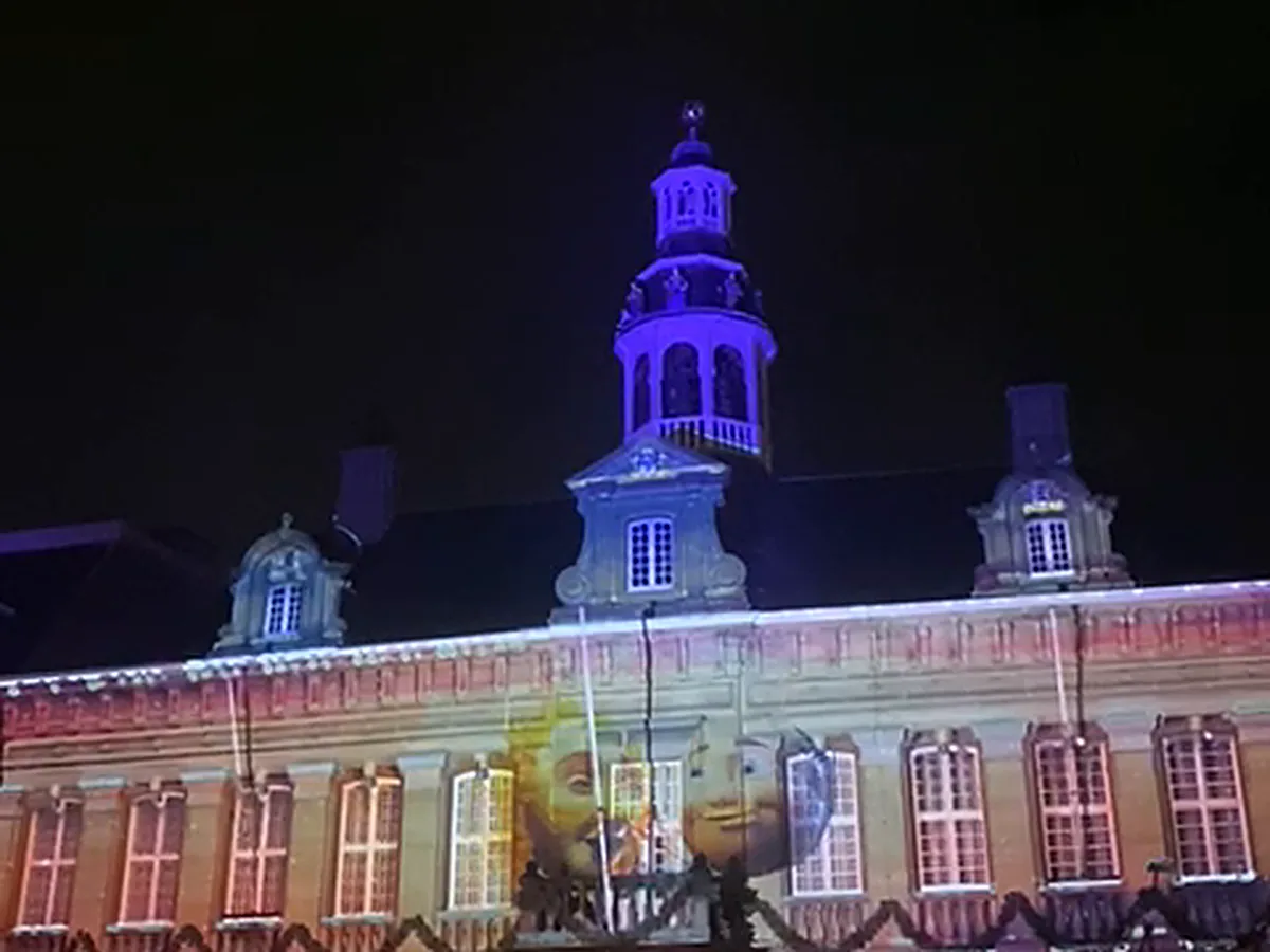 Historisch stadhuis van Roermond met videomapping: een geprojecteerde zon en maan op de gevel en de paars verlichte toren, tijdens ROERMONDVOL Licht