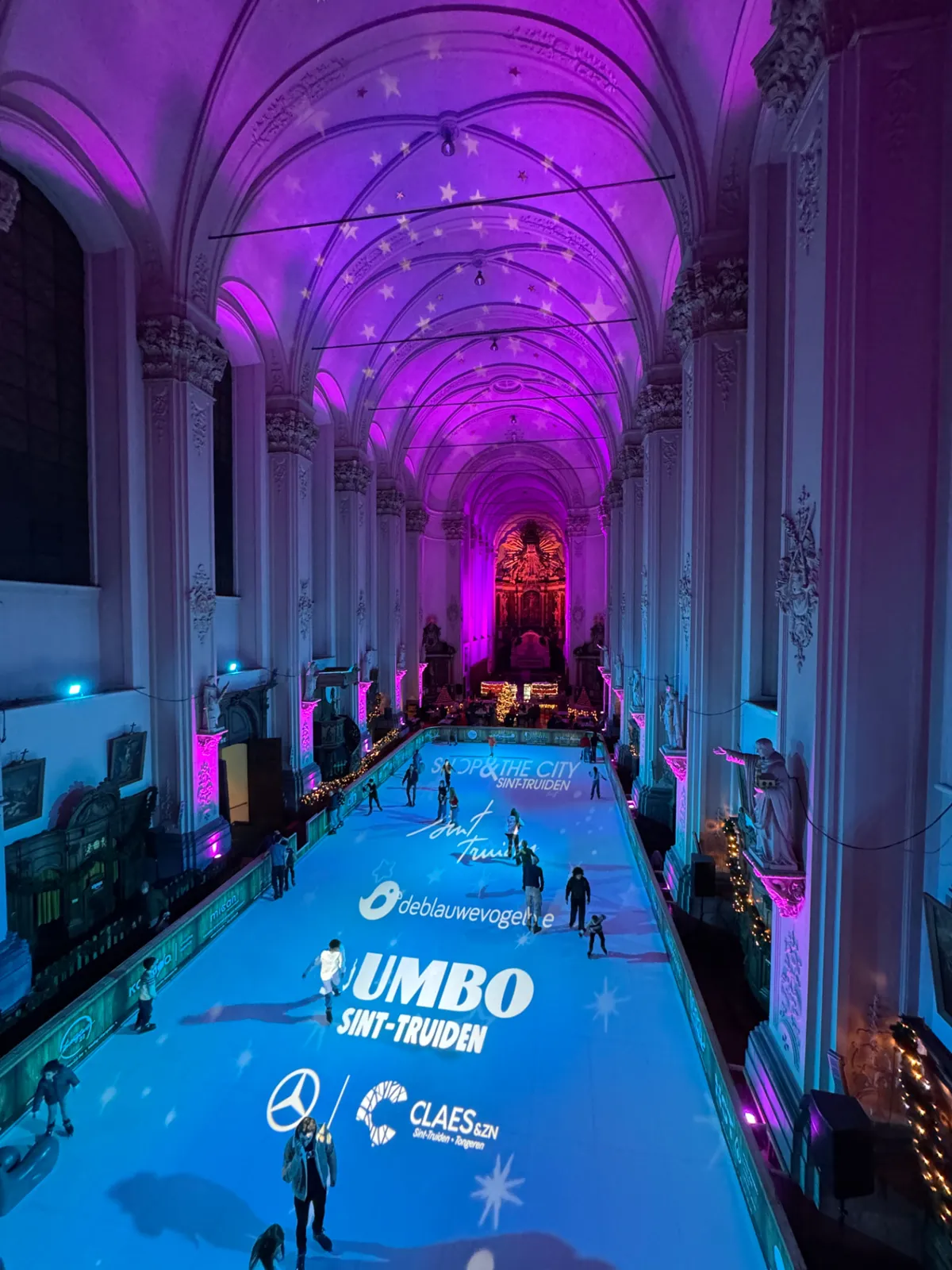 Indoor schaatsbaan in de Minderbroederskerk van Sint-Truiden met sterren op het gewelf en sponsorlogo's op het ijs